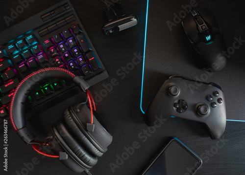 gamer workspace concept, top view a gaming gear, mouse, keyboard, joystick, headset, mobile joystick and mouse pad on black table background with RGB color.