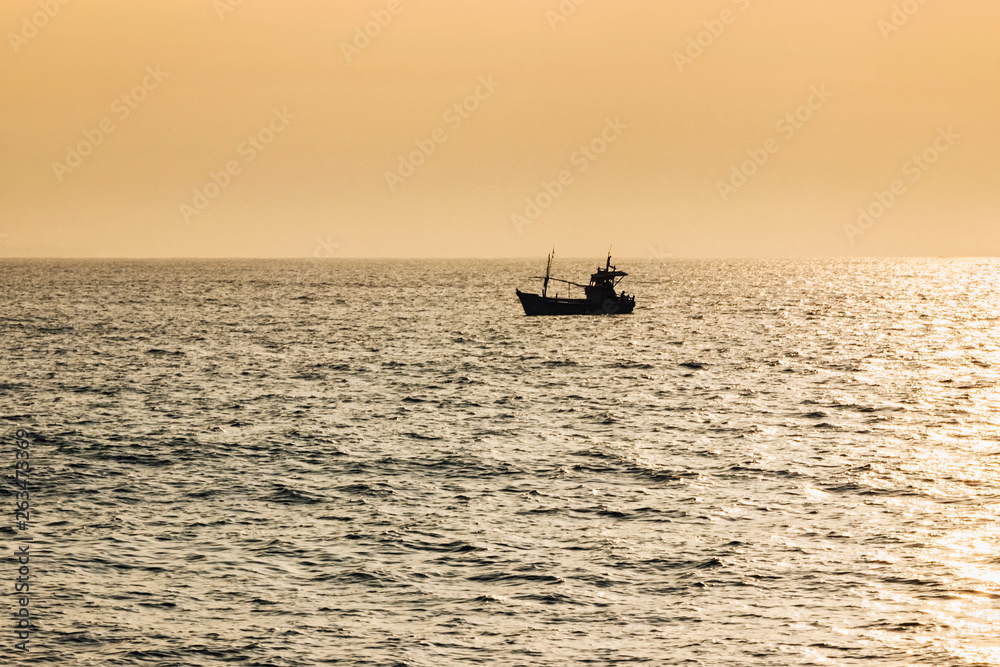 fishing boat in ocean with golden sunshine at sunrise