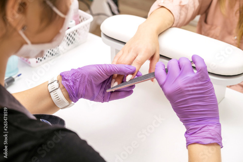 Manicurist work on a woman client hands, make her nails look beautiful. Salon procedure in process. Professional works in gloves for sterility