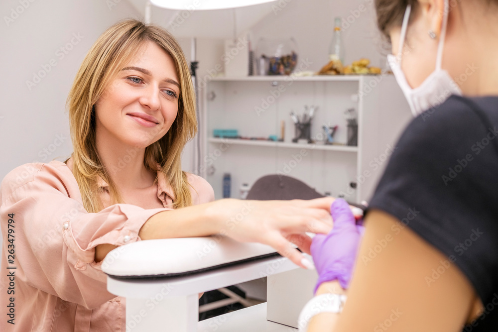 Manicurist work on a woman client hands, make her nails look beautiful. Salon procedure in process. Professional works in gloves for sterility Manicurist work on a woman client hands, make her nails look beautiful. Salon procedure in process. Professional works in gloves for sterility
