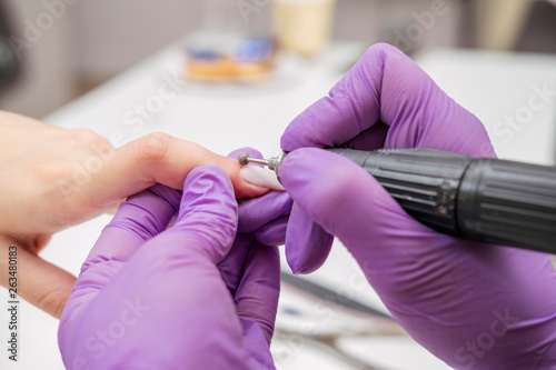 Manicurist work on a woman client hands, make her nails look beautiful. Salon procedure in process. Professional works in gloves using drill for sterility