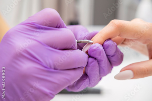 Manicurist work on a woman client hands, make her nails look beautiful. Salon procedure in process. Professional works in gloves for sterility