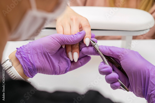 Manicurist work on a woman client hands  make her nails look beautiful. Salon procedure in process. Professional works in gloves for sterility