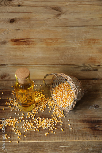 corn oil in a bottle with a basket of corn kernels scattered on a wooden rustic background with copy space for text. Top view.Vertical photo.