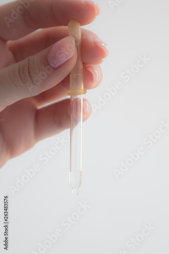 medical ordinary pipette in a woman's hand, clear liquid, beautiful female fingers, a drop on the pipette