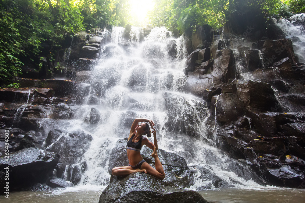 Woman practices yoga near waterfall in Bali, Indonesia Woman practices yoga near waterfall in Bali, Indonesia