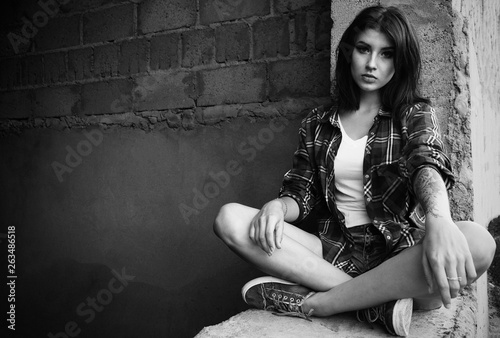 Girl in an abandoned building sits on concrete in jeans with a tattoo