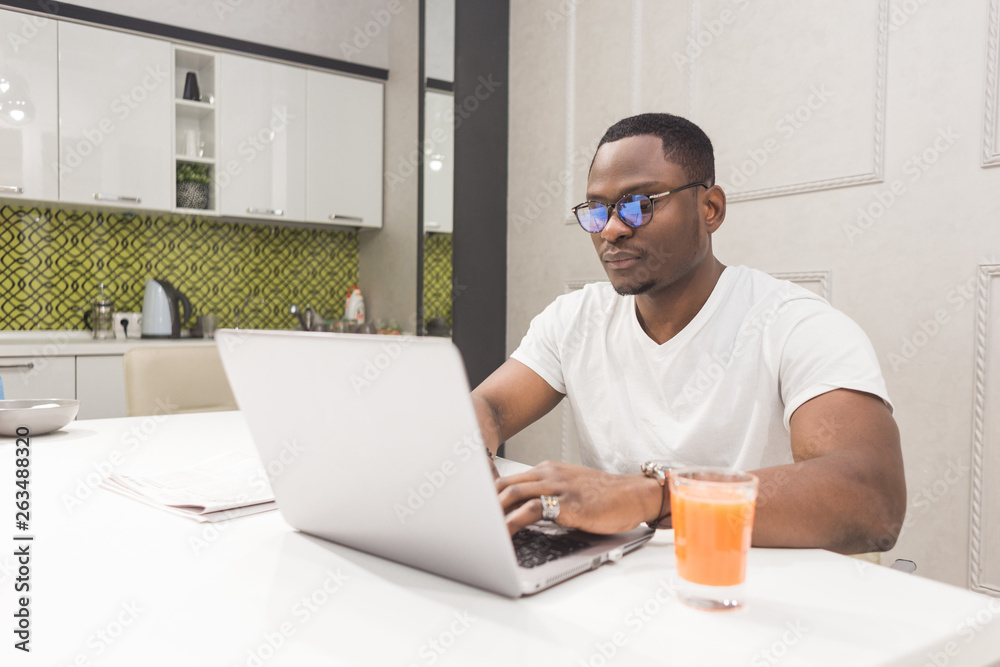 Young African American businessman working on a laptop in the kitchen in a modern interior.