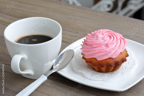 Cream cake and cup of coffee. Cake lies on a saucer. Near a coffee spoon.