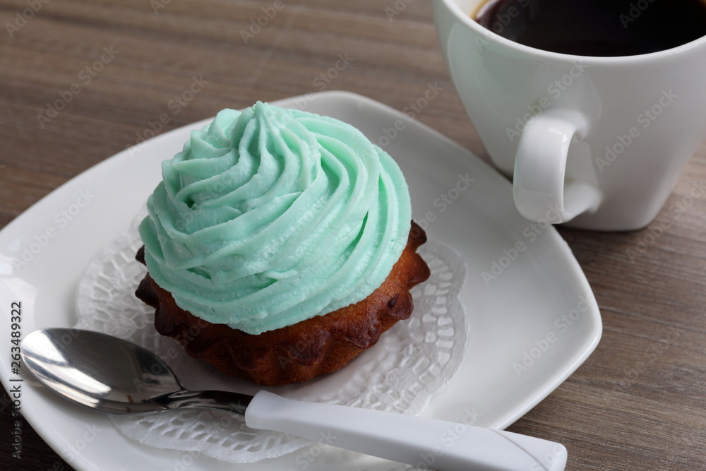 Cream cake and cup of coffee. Cake lies on a saucer. Near a coffee spoon.