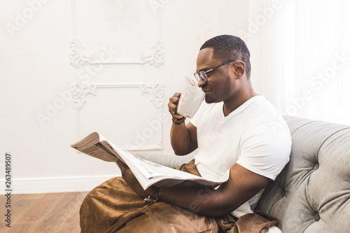 Young African American man, covered with a blanket reading a newspaper at home.