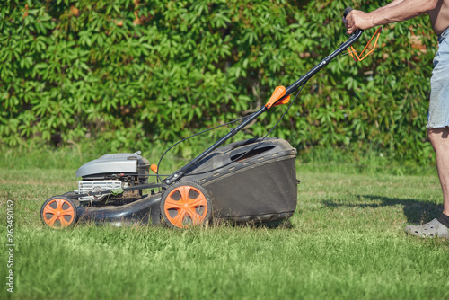 European man is working on the personal plot, he is using lawn mower.