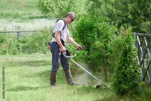 Man is using grass trimmer on his countryside yard.