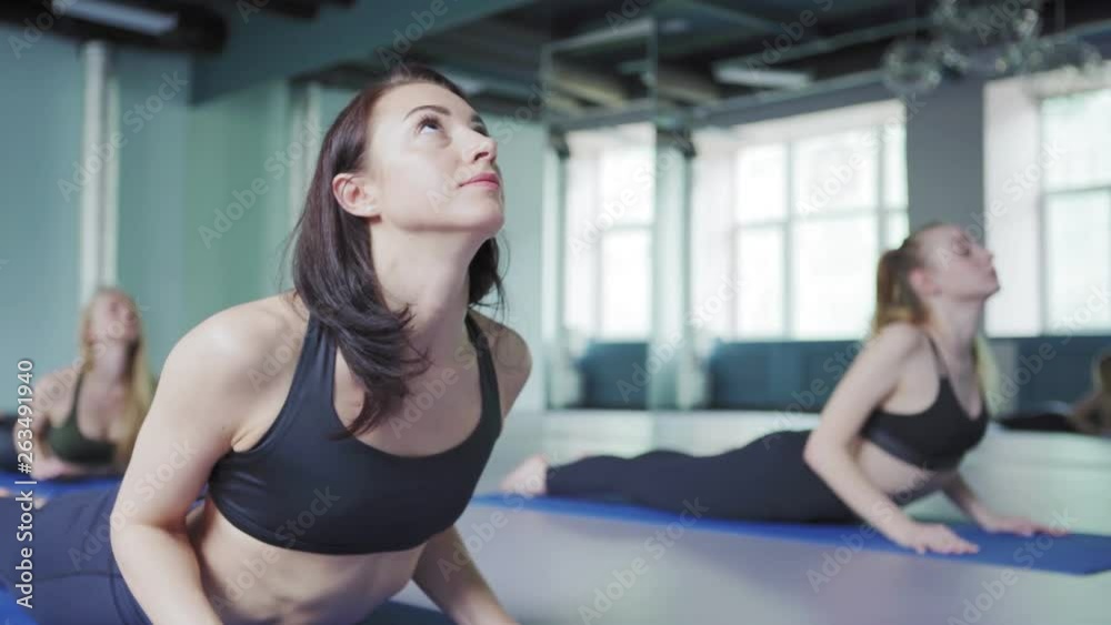 Tilt up and down shot of three women practicing yoga cobra pose on mats. Focus on yoga instructor showing asana to her clients Tilt up and down shot of three women practicing yoga cobra pose on mats. Focus on yoga instructor showing asana to her clients