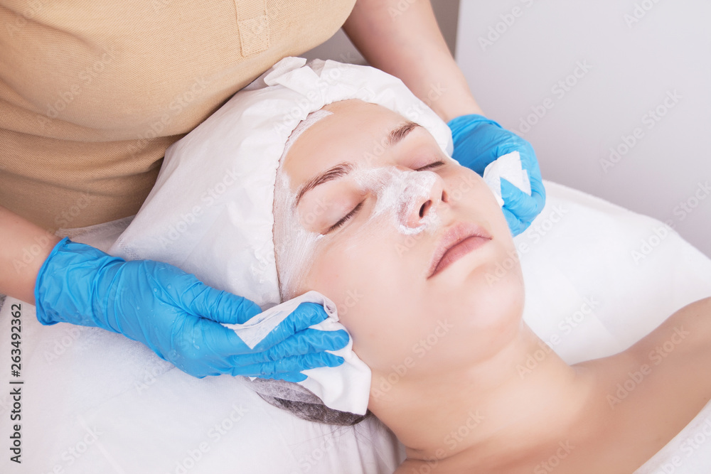 The beautician wipes the mask from the face of a young woman after a cosmetological procedure.