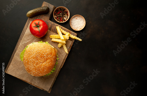 Delicious homemade hamburger with beef, lettuce, cheese, cucumber and french fries on stone background, top view with copy space for your text.