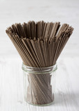 Organic buckwheat soba noodles in a glass jar over white wooden background, side view. Close-up.