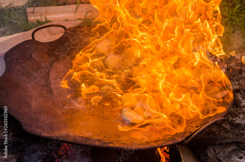 Fried bbq potatoes in a large frying pan on an open fire with smoke.