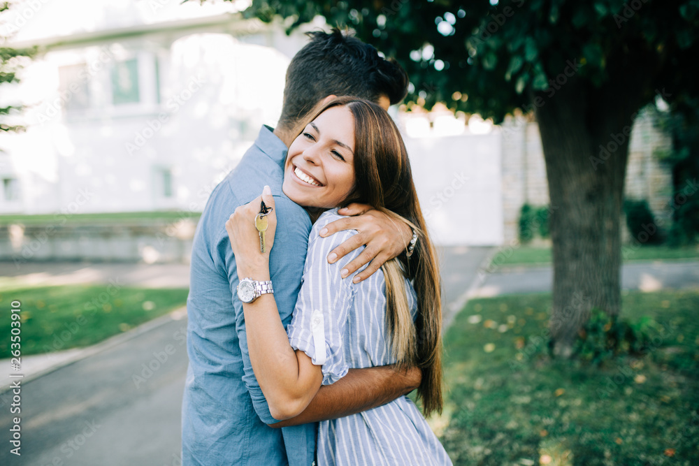 Happy young couple with key standing outside in front of their new home.