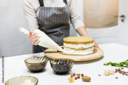 Confectioner with pastry bag squeezing cream on cake at kitchen. The concept of homemade pastry, cooking cakes.