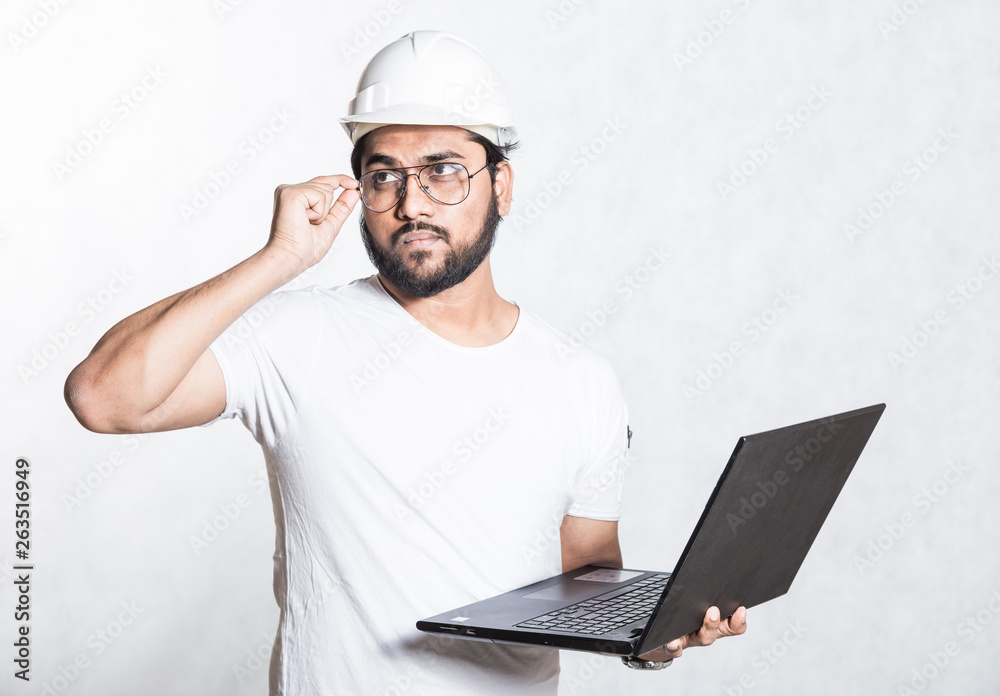 Young builder engineer in glasses and a white safety helmet, stands with an open laptop. Young builder engineer in glasses and a white safety helmet, stands with an open laptop.