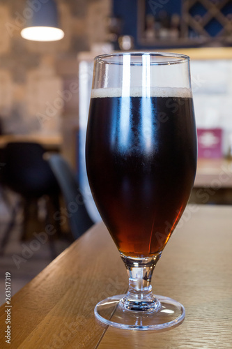 Glass goblet of cold stout beer standing on table against wooden background