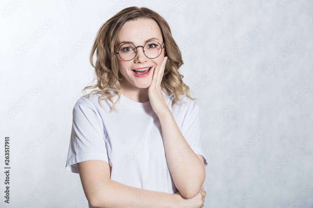 Amazed young woman looks with a smile and surprise, presses hand to cheek, being shocked to hear good news. Amazed young woman looks with a smile and surprise, presses hand to cheek, being shocked to hear good news.