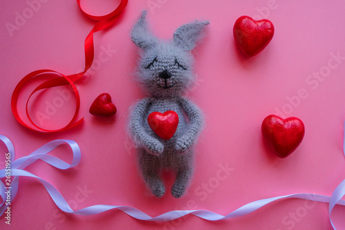 soft toy hare on a pink background surrounded by hearts and ribbons photo