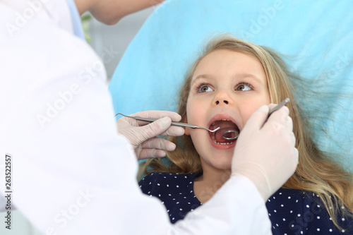 Little baby girl sitting at dental chair with open mouth and feeling fear during oral check up while doctor. Visiting dentist office. Medicine concept