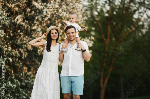 Beautiful young parents and their cute little son have fun near flowering trees, happy family