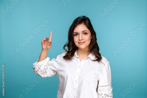 Pretty brunette girl pointing something by finger isolated over the blue background