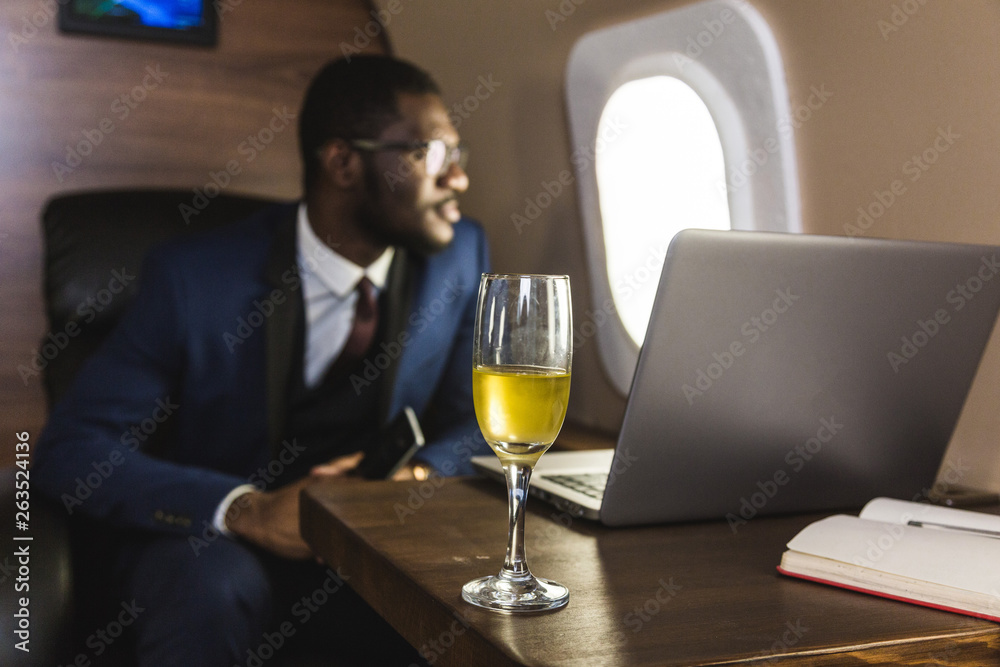 Attractive and successful African American businessman with glasses working on a laptop while sitting in the chair of his private jet.