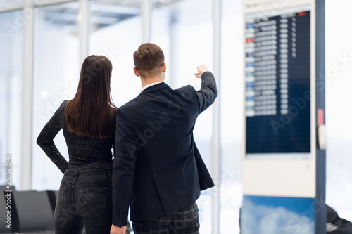 Young couple in international airport looking at the flight information board, checking her flight