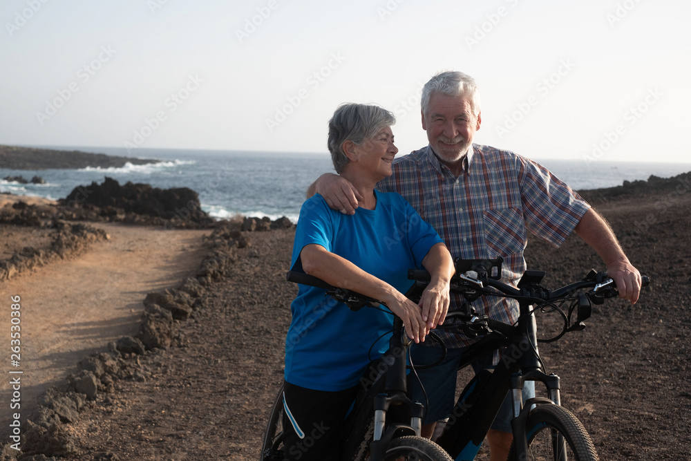 Naklejka premium Freedom and happiness for a senior couple of retired persons enjoying bicycling along the footpath, ocean on the background