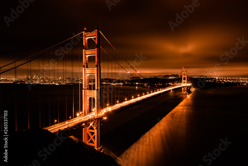The golden gate bridge in San Francisco California taken on a cool summer night. The skyline of the city glows in the distant horizon as the building lights provide a urban background to the scene