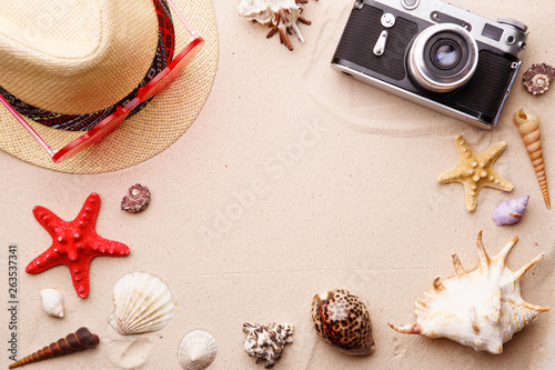 Beach accessories - sunglasses, hat and camera on sand witn shells and seastar.