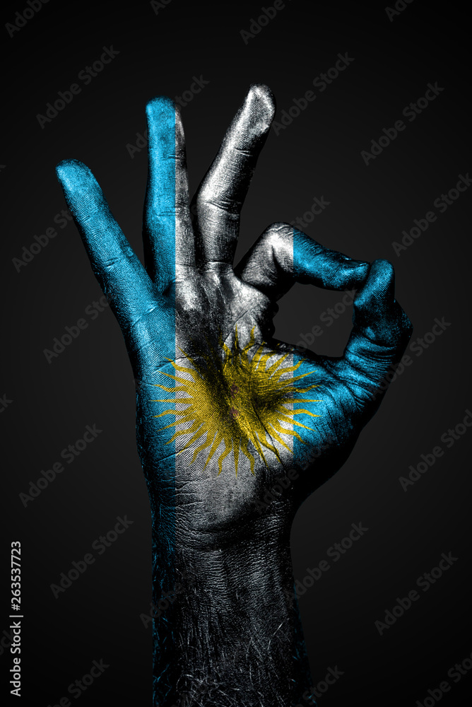 A hand with the painted flag of Argentina shows an OK sign on a dark background.