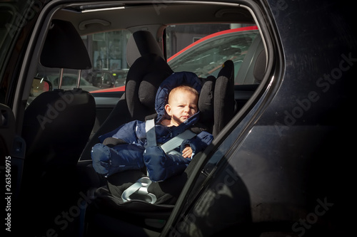 Wallpaper Mural Unhappy, sad child sitting in a child car seat on the second row of a black car. He is dressed in warm overalls of dark blue color. Torontodigital.ca