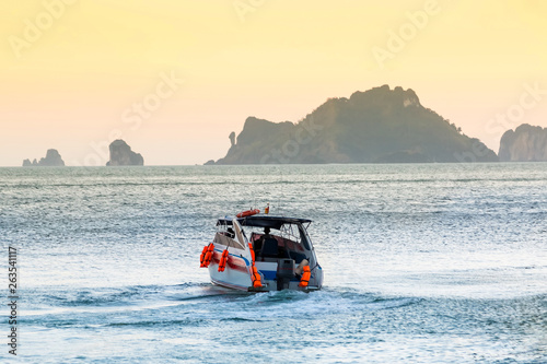 Coast Guard motorboat sails from shore. Sunset sky and mountains in the background. Man drives a lifeguard ship