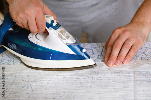 Housework and household concept. Man is ironing textile on ironing board at home. Blue iron in man hand.