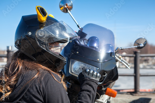 Biker girl in helmet with mask clenches fist while sitting in front of plastic front cowl with headlight of her motorcycle