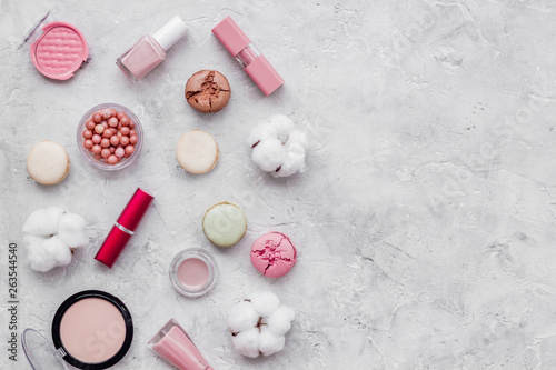 Make-up artist desk with powder, nail polish, decorative cosmetics and macaroon cookies stone background top view mokeup