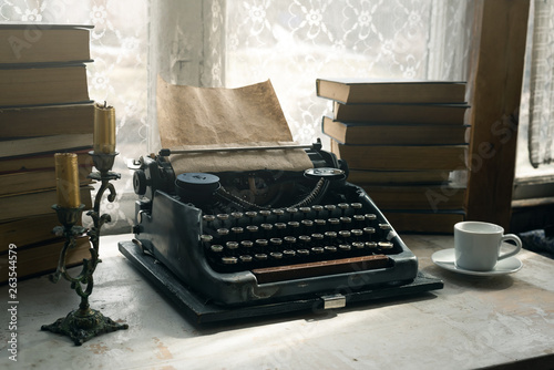 Typewriter, stack of books, candle and a cup of coffee or tea on a writer table background.