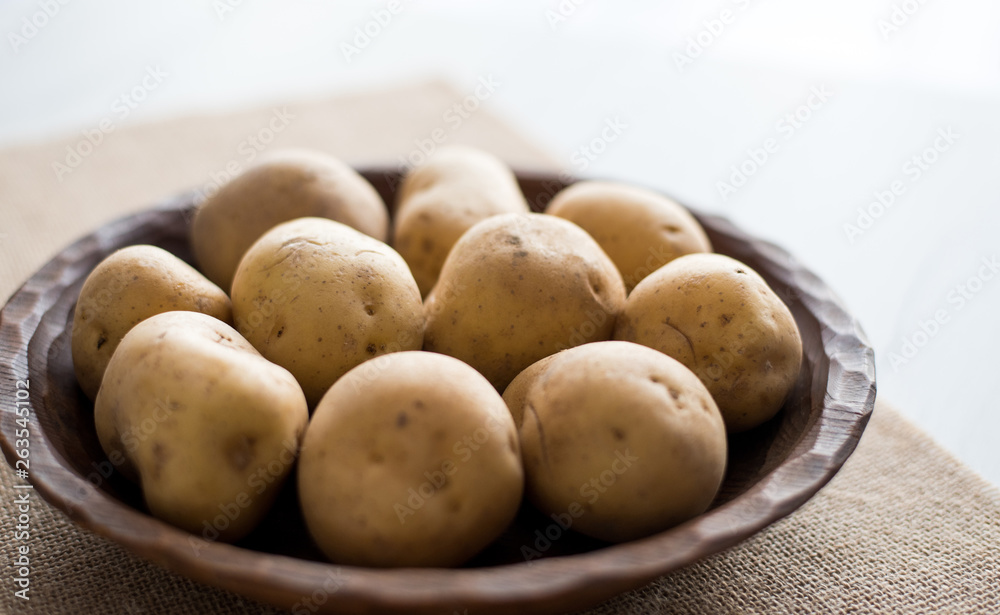Raw potatoes in rustic wooden plate, on bright background. Organic agriculture & food concept. Raw potatoes in rustic wooden plate, on bright background. Organic agriculture & food concept.