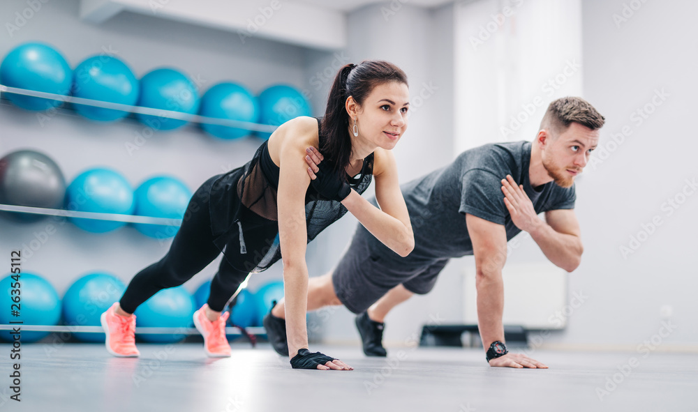 Young couple doing push-ups from the floor on one hand together on the background of fitness balls. Sporty male and female in sportswear training in the sports club.
