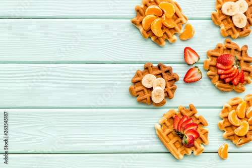 Homemade Viennese waffles with strawberry, tangerine and banana topings on mint green wooden background top view makeup