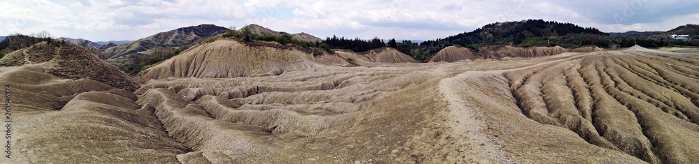 Panoramic view of an arid landscape created by the Mud Volcanoes in Berca, Romania. A mud volcano or mud dome is a landform created by the eruption of mud or slurries, water and gases