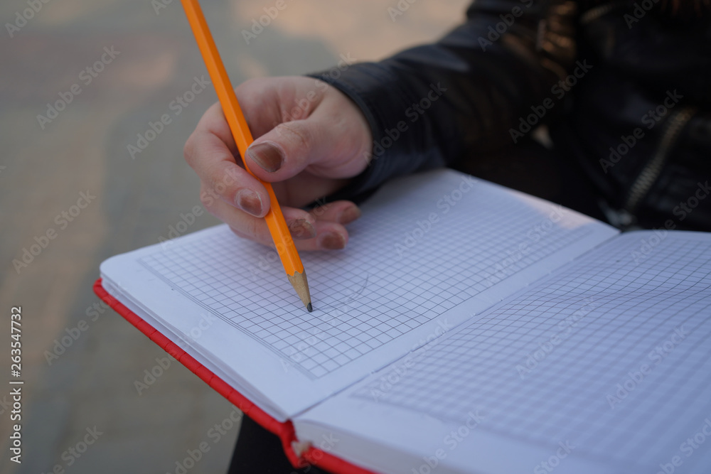 A woman with a notebook in his hands in the Park. Beautiful female student is writing her ideas and thoughts into the notebook sitting on the bench in the park A woman with a notebook in his hands in the Park. Beautiful female student is writing her ideas and thoughts into the notebook sitting on the bench in the park