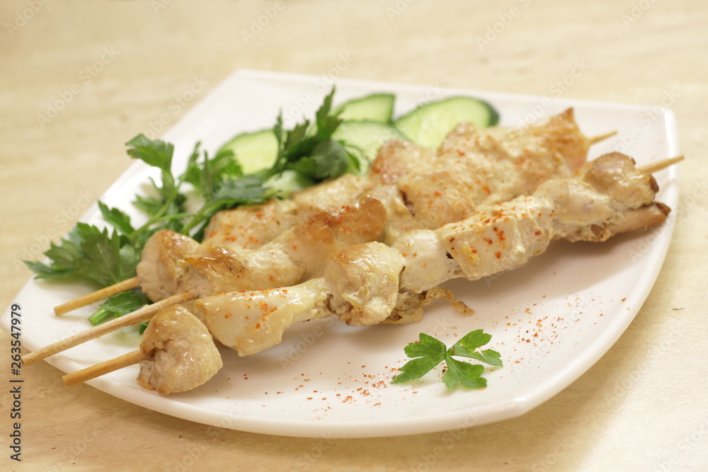 Baked chicken fillet on wooden skewers with cucumber and dill. Barbecue from pieces of chicken on wooden skewers.