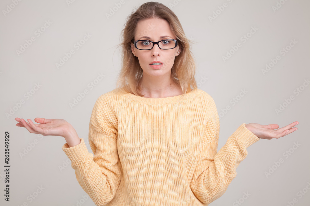 portrait of young blond woman with surprised emotion on her face. looking at the camera, notices something unexpected,wearing yellow sweater and glasses. poses against grey background.face expression portrait of young blond woman with surprised emotion on her face. looking at the camera, notices something unexpected,wearing yellow sweater and glasses. poses against grey background.face expression